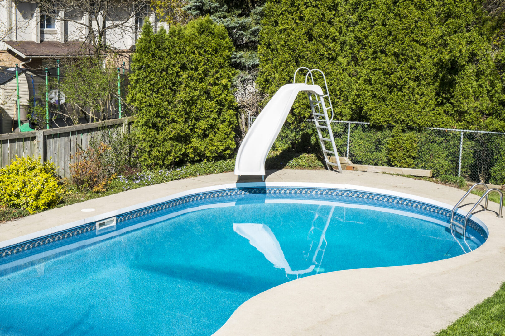 White water slide by a swimming pool in a backyard.